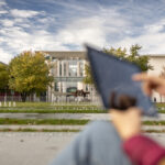 Blick aufs Kanzleramt in Berlin von Außen, im Vordergrund sieht man unscharf eine Person, die mit einem Tablet hantiert