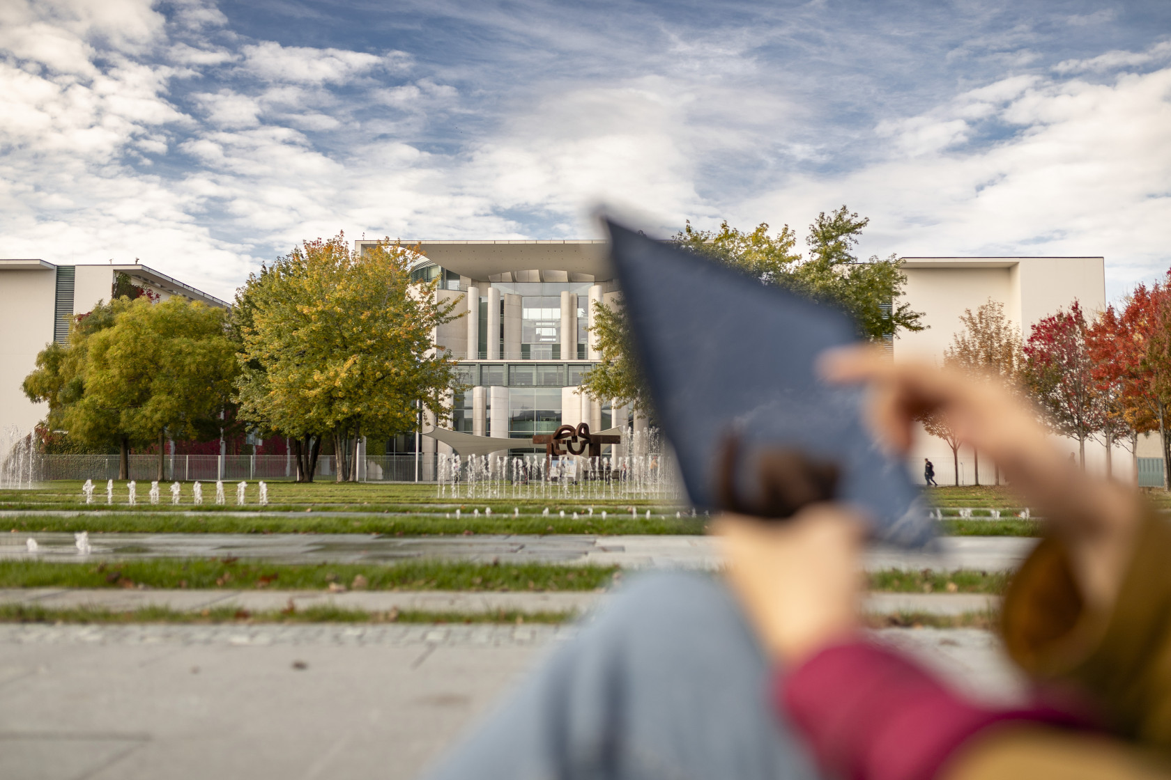 Blick aufs Kanzleramt in Berlin von Außen, im Vordergrund sieht man unscharf eine Person, die mit einem Tablet hantiert