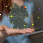 Hand und Oberkörper einer jungen Frau, die ein Tablet und eine einmontierte schwebende Deutschlandkarte mit vernetzten Punkten hält.