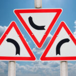 Drei Verkehrsschilder (Abbiegen) gegen blauen Himmel aufgenommen