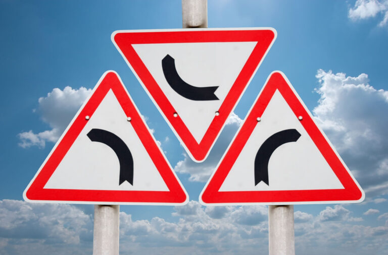 Drei Verkehrsschilder (Abbiegen) gegen blauen Himmel aufgenommen