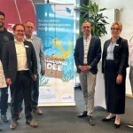 Mehrere Menschen stehen vor einem Aufsteller mit der Aufschrift „Startuphafen SH“.