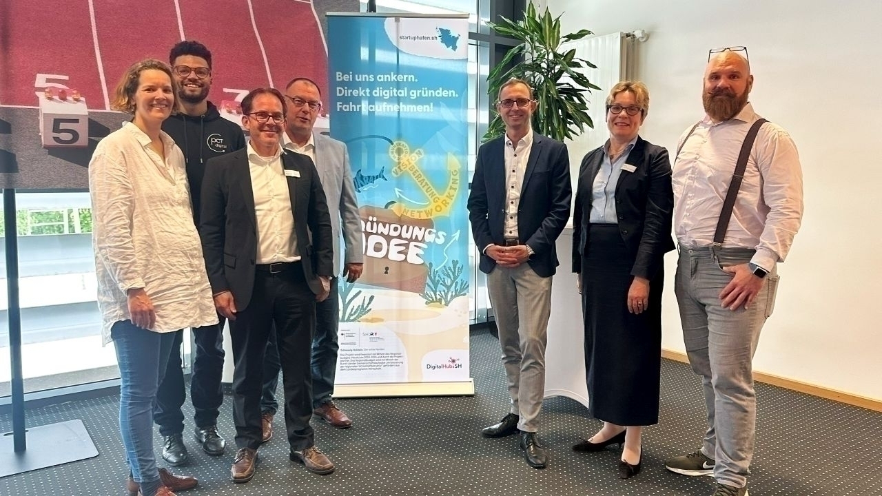 Mehrere Menschen stehen vor einem Aufsteller mit der Aufschrift „Startuphafen SH“.